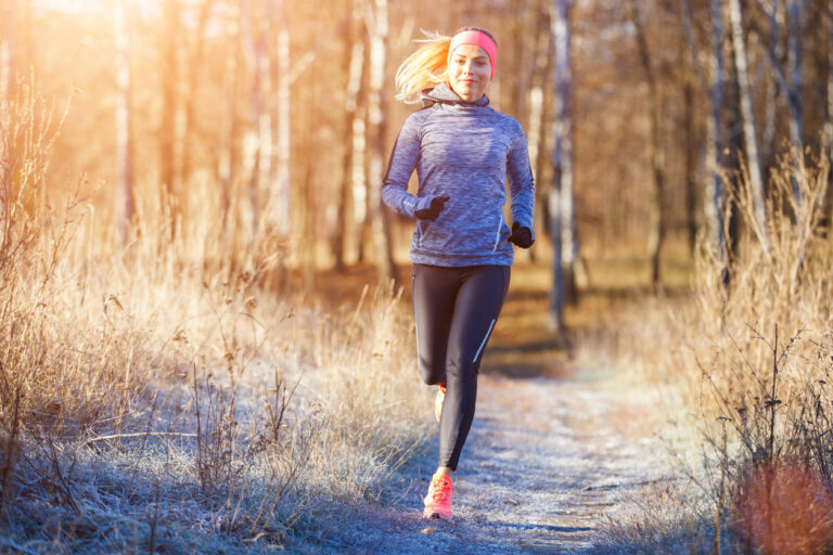 Young slim girl running in the park in early winter. Attractive woman jogging on snowy trail